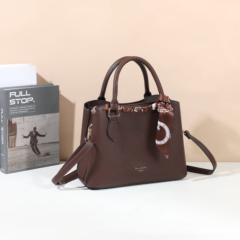 Sac à main La Mystérieuse coffee posé sur une table blanche près d’un livre, devant un mur pêche – visuel d’ambiance créé avec l’IA – Gallantry Paris