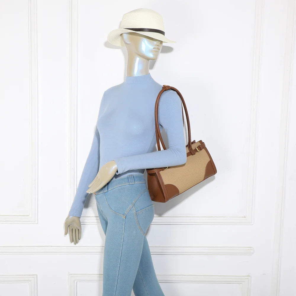 Sac Amarante taupe foncé porté à l’épaule par une femme, format allongé qui se glisse sous le bras
