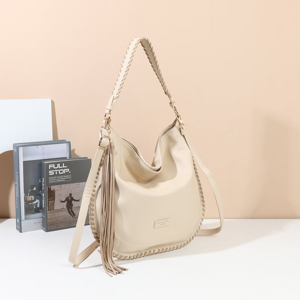Sac à main hobo Céleste beige avec anse tressée et pompon à franges, mis en scène dans un décor – visuel d’ambiance créé avec l’IA – Gallantry Paris