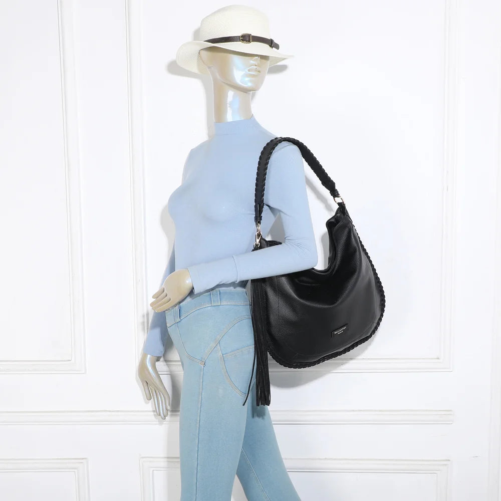 Sac Céleste noir porté par une femme : anse tressée à l’épaule, pompon à franges le long de la silhouette – réf. JC-53006