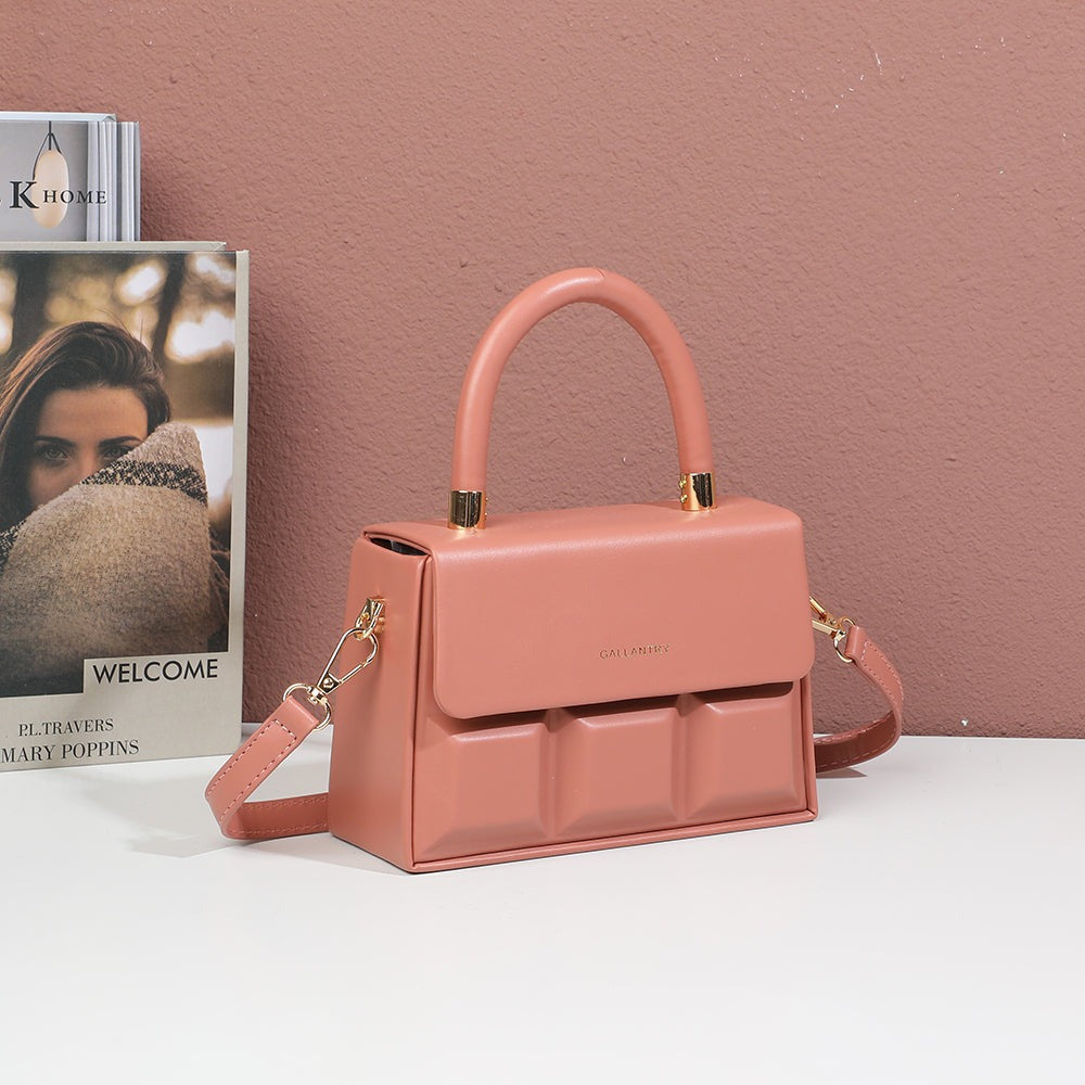 Sac à main ChocoLuxe rose foncé posé sur une table devant des livres et un mur rosé – visuel d'ambiance créé avec l'IA – Gallantry Paris
