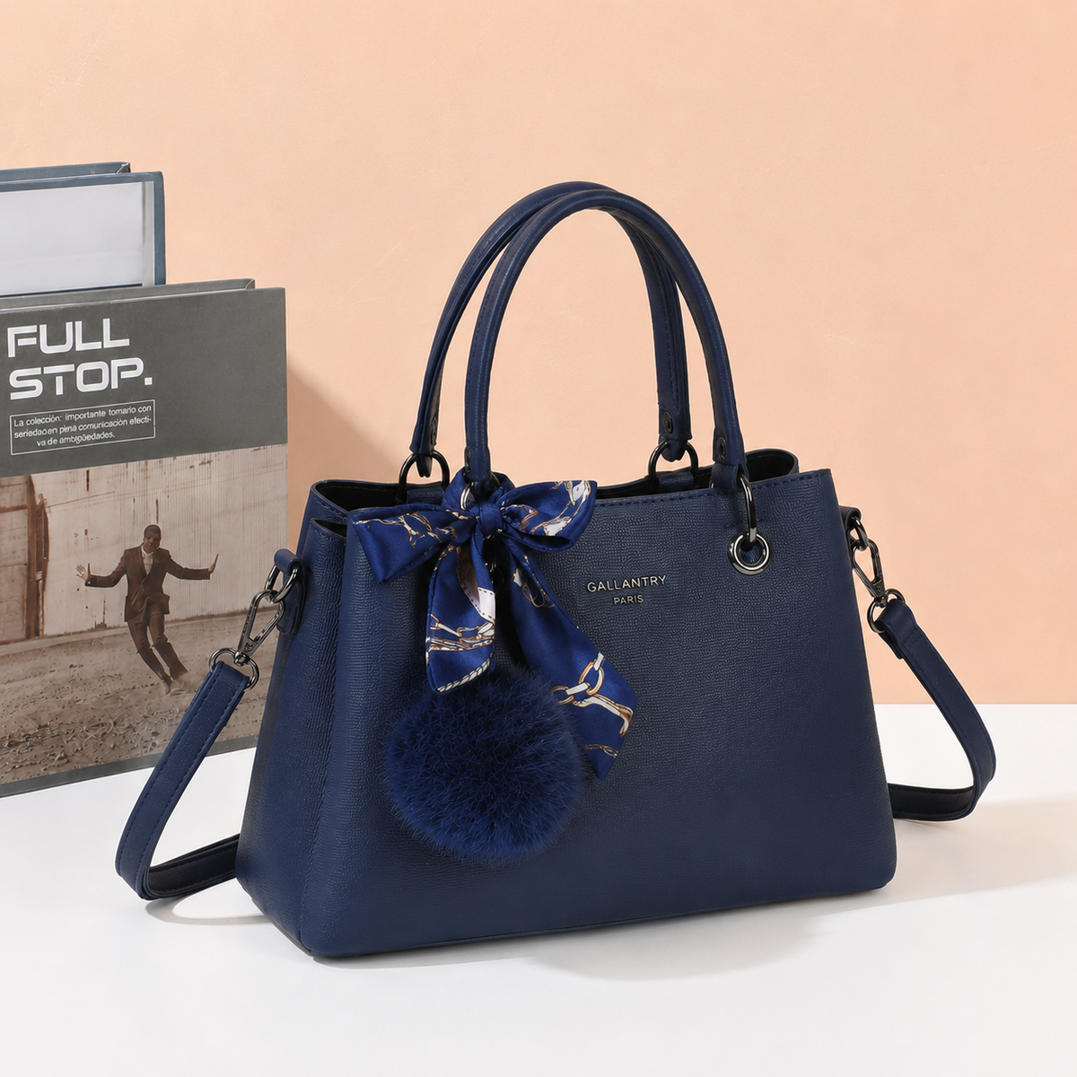 Sac à main La Coquette bleu foncé à pompon et foulard, posé près de livres – visuel d'ambiance créé avec l'IA – Gallantry Paris