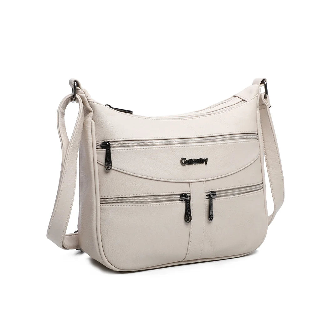 La Elya beige vue de trois quarts : silhouette arrondie, plaque logo en métal foncé et bandoulière réglable – réf. Z-83001