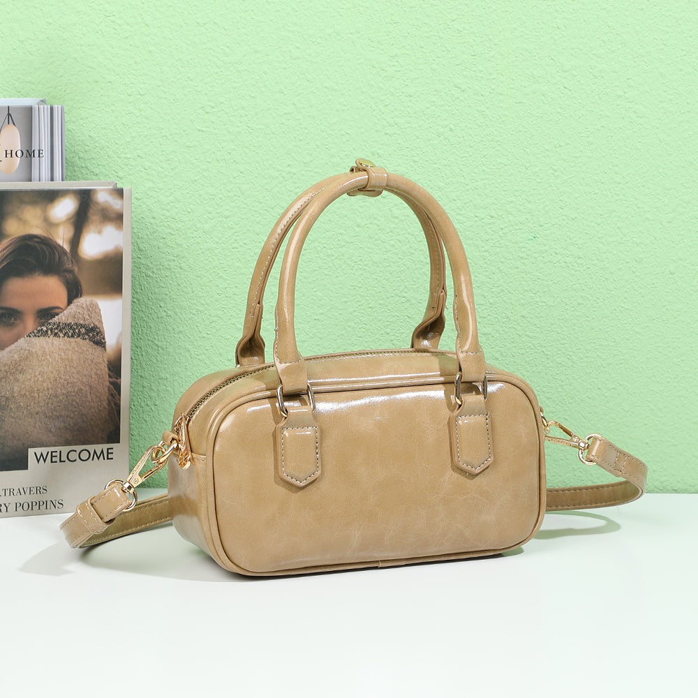 Mini Glossy taupe posé sur une table blanche devant un livre et un mur vert d’eau – visuel d’ambiance créé avec l’IA – Gallantry Paris
