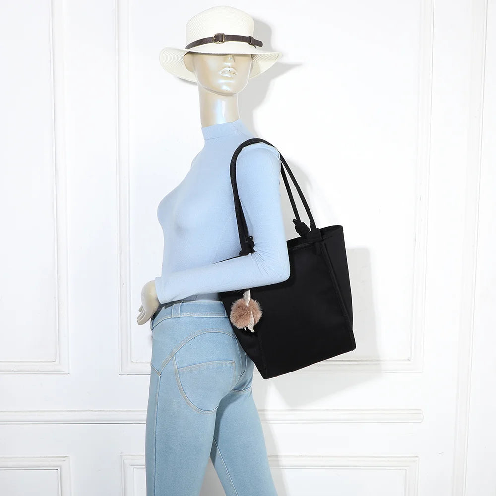 Sac cabas Noéva noir porté à l’épaule par une femme, grâce à ses deux longues anses nouées – réf. M-9455
