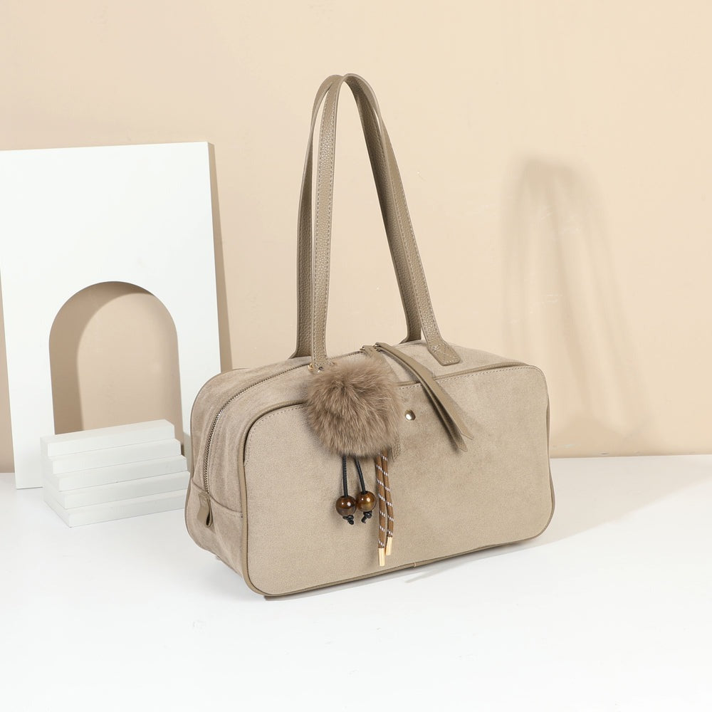 Sac Ovalia Taupe foncé en suédine avec son pompon, posé dans un décor intérieur – visuel d’ambiance créé avec l’IA – Gallantry Paris