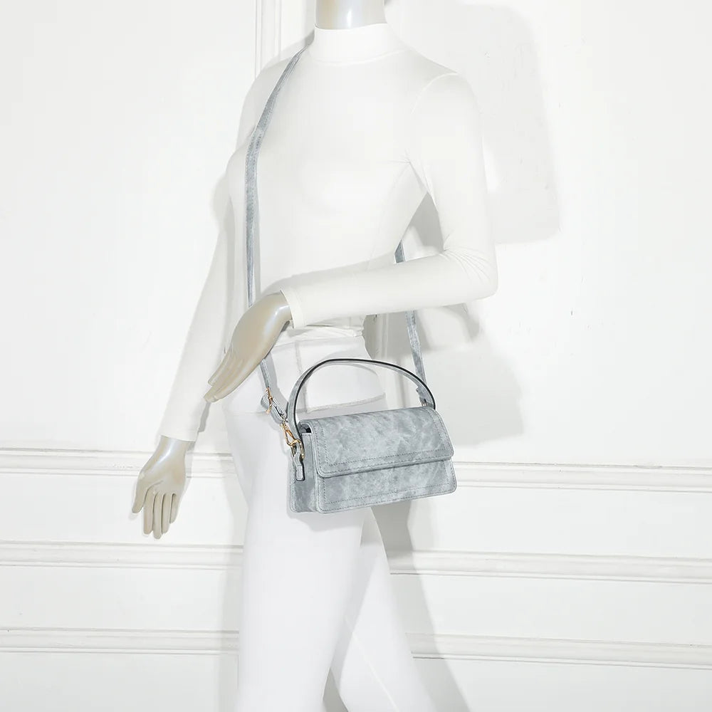 Rosino bleu porté à l’épaule par une femme, sac à rabat compact tenu par son anse courte – réf. C-0167-1